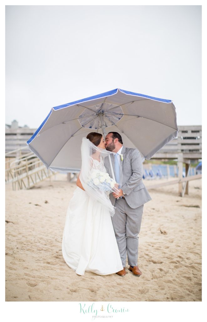 A bride and groom kiss under an umbrella. 