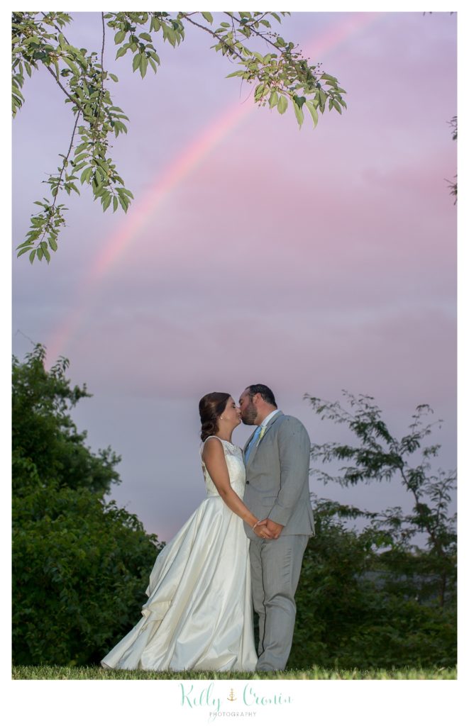 A bride and groom kiss under a rainbow. 