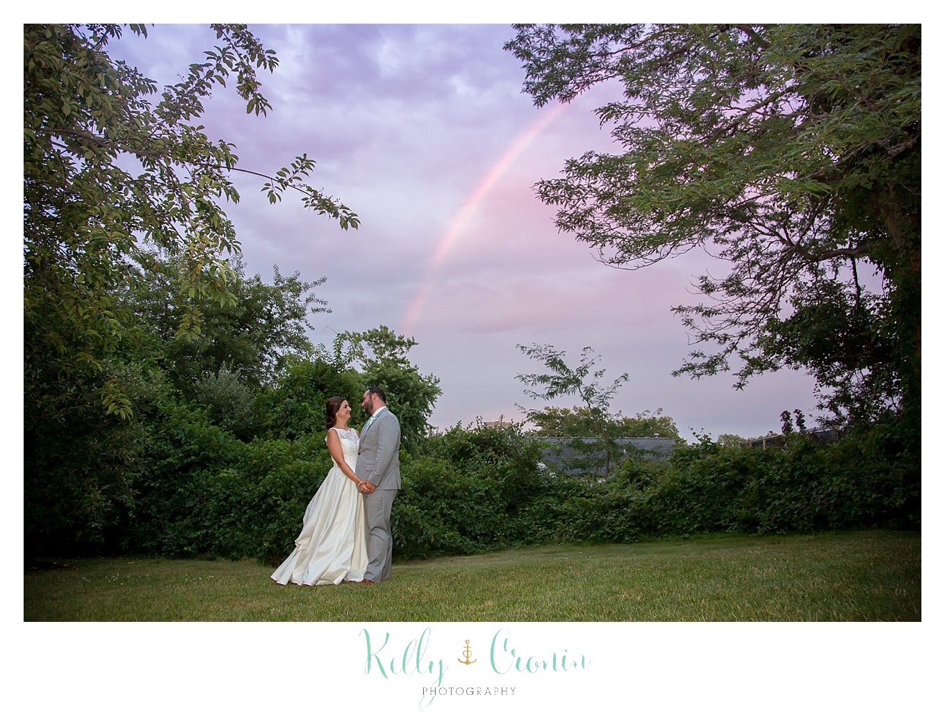 A groom kisses his bride under a bright rainbow.