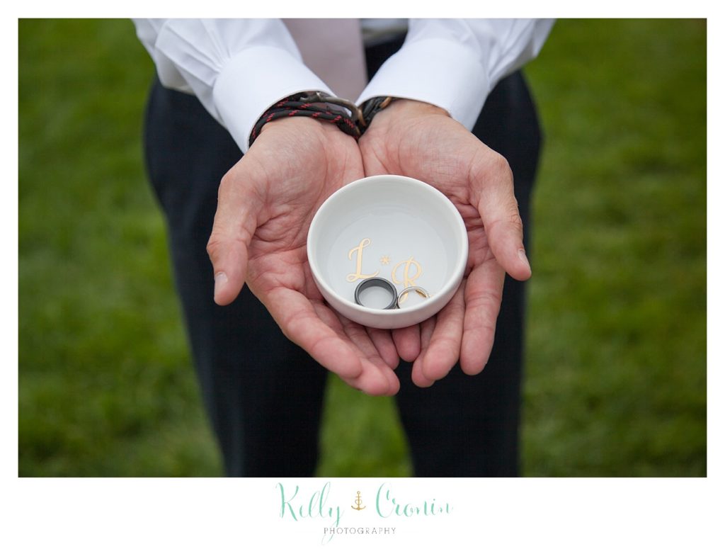 A groom holds a bowl with wedding rings inside. 