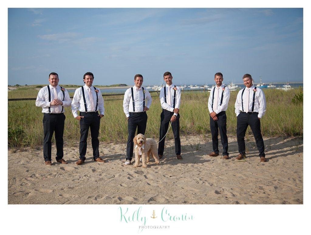 Groomsmen stand with their hands in their pockets on the beach. 