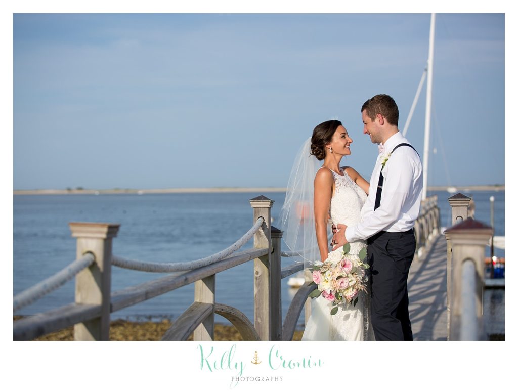 A bride and groom stand on a pier. 