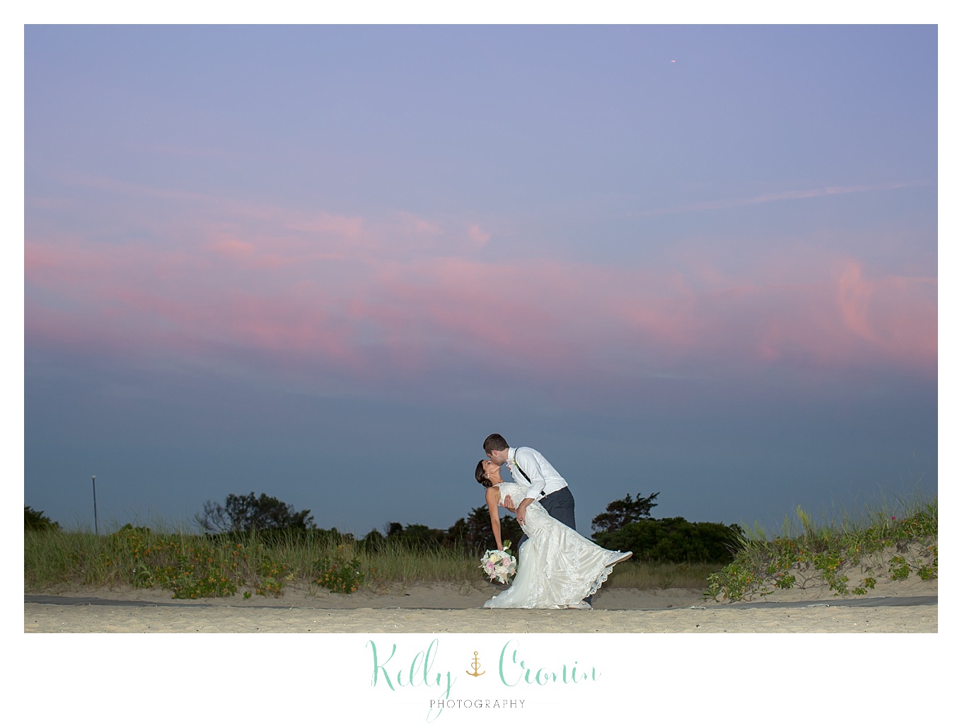A groom kisses his bride in front of a sunset.