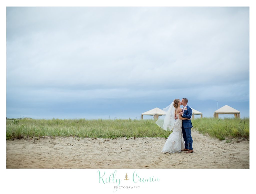 A bride and groom kiss on the beach. 