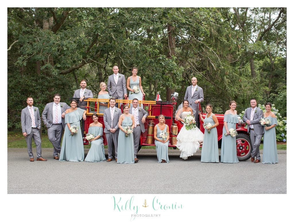 A wedding party stands in front of an antique fire engine. 