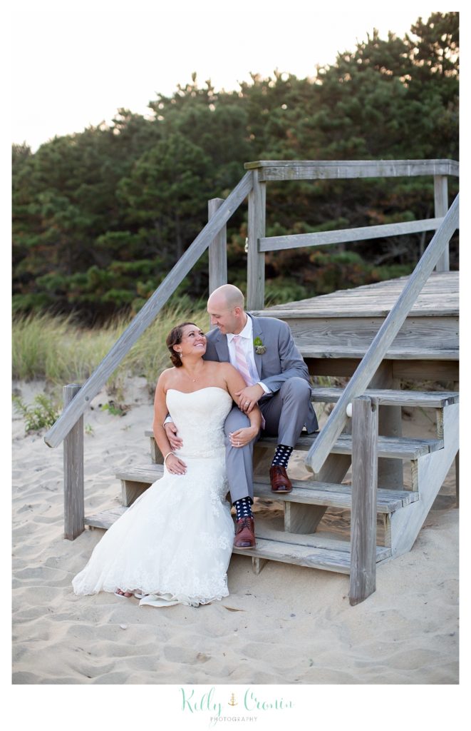 A bride and groom sit on the steps of an old pier. 