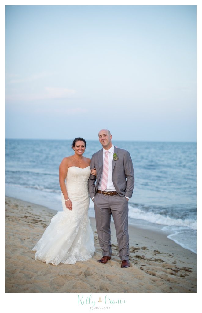 A bride and groom walk along the shore. 
