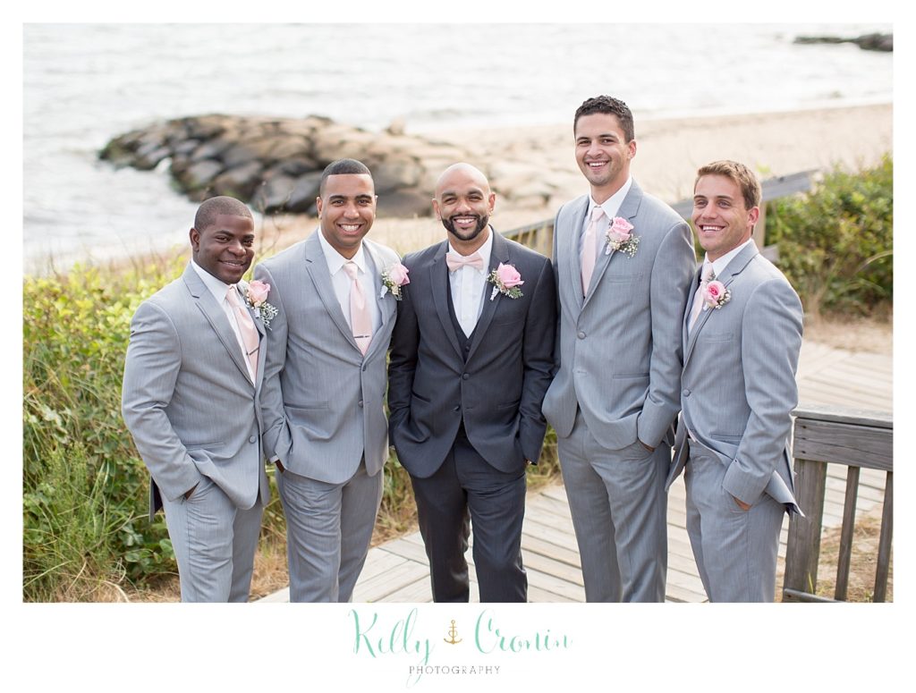 Some groomsmen stand in front of the beach together. 