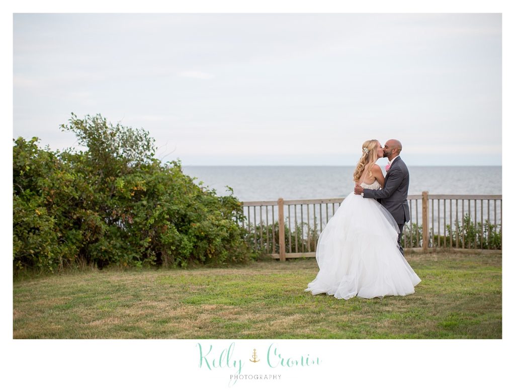 A bride and groom kiss on the seashore. 