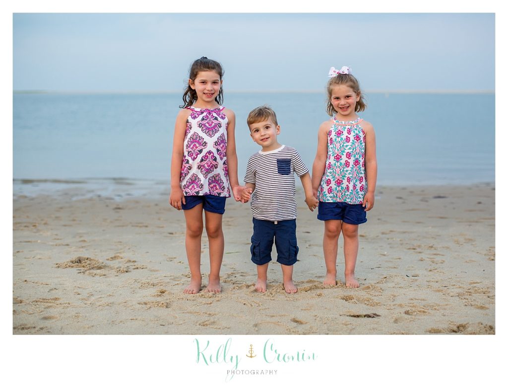 Three siblings stand on the beach for some family pictures. 