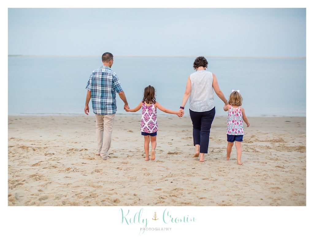 Two parents hold hands with their two small daughters to walk on the beach. 
