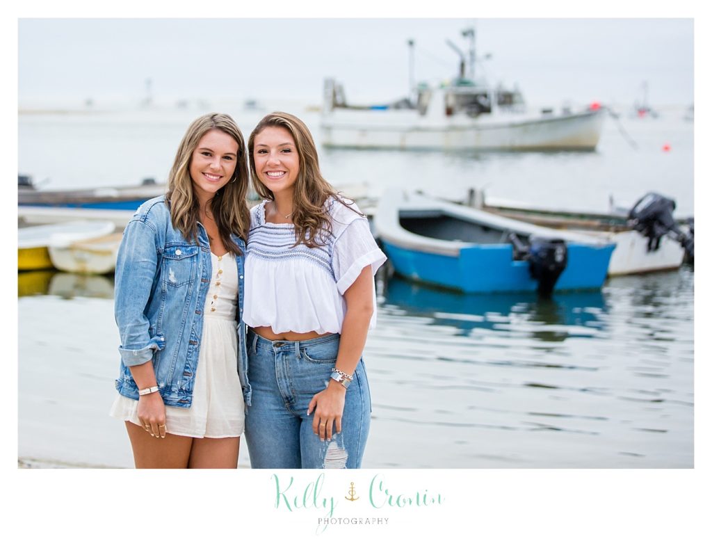 Two sisters stand in front of a boat on the water. 