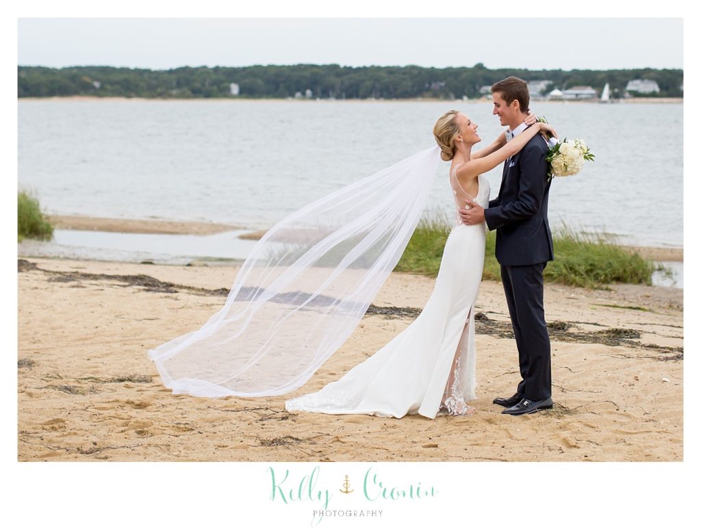 A bride's veil blows in the wind as she has her arms around her groom.