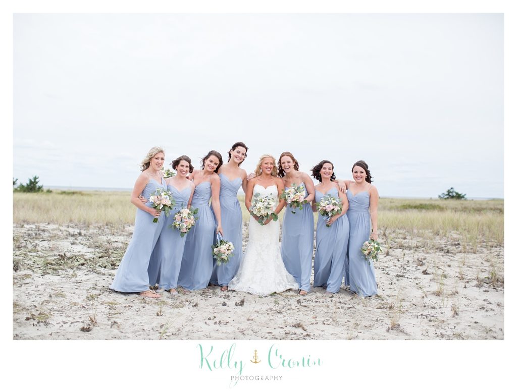 A bride laughs on the beach with her bridesmaids. 