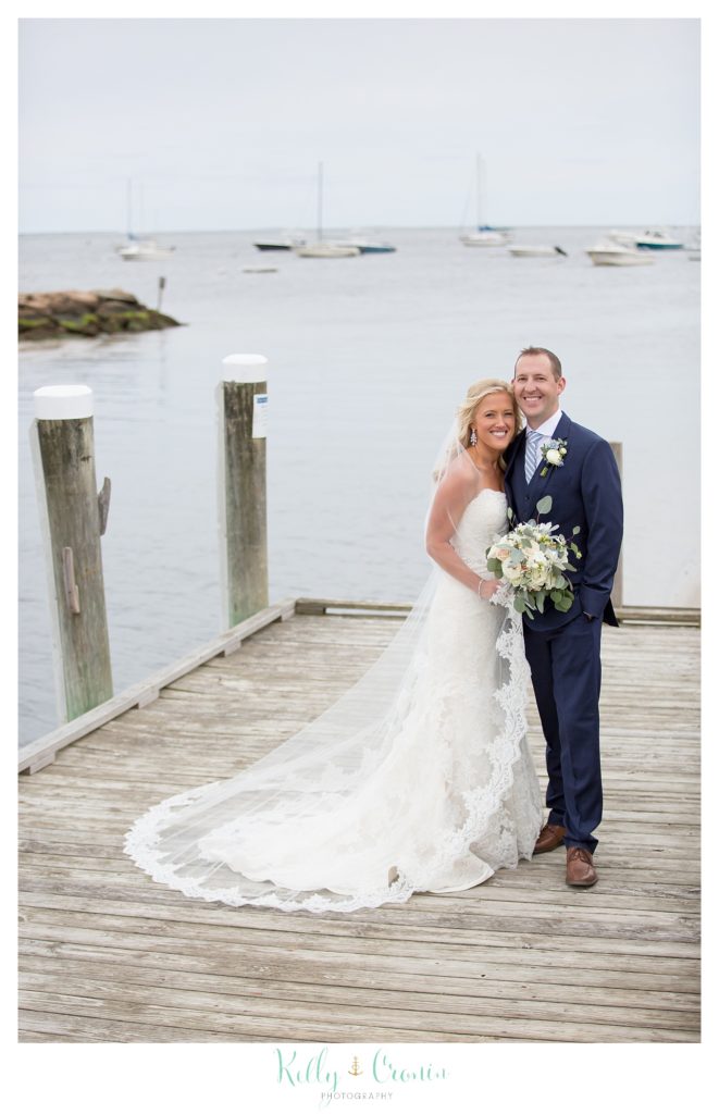 A bride and groom stand on a pier. 