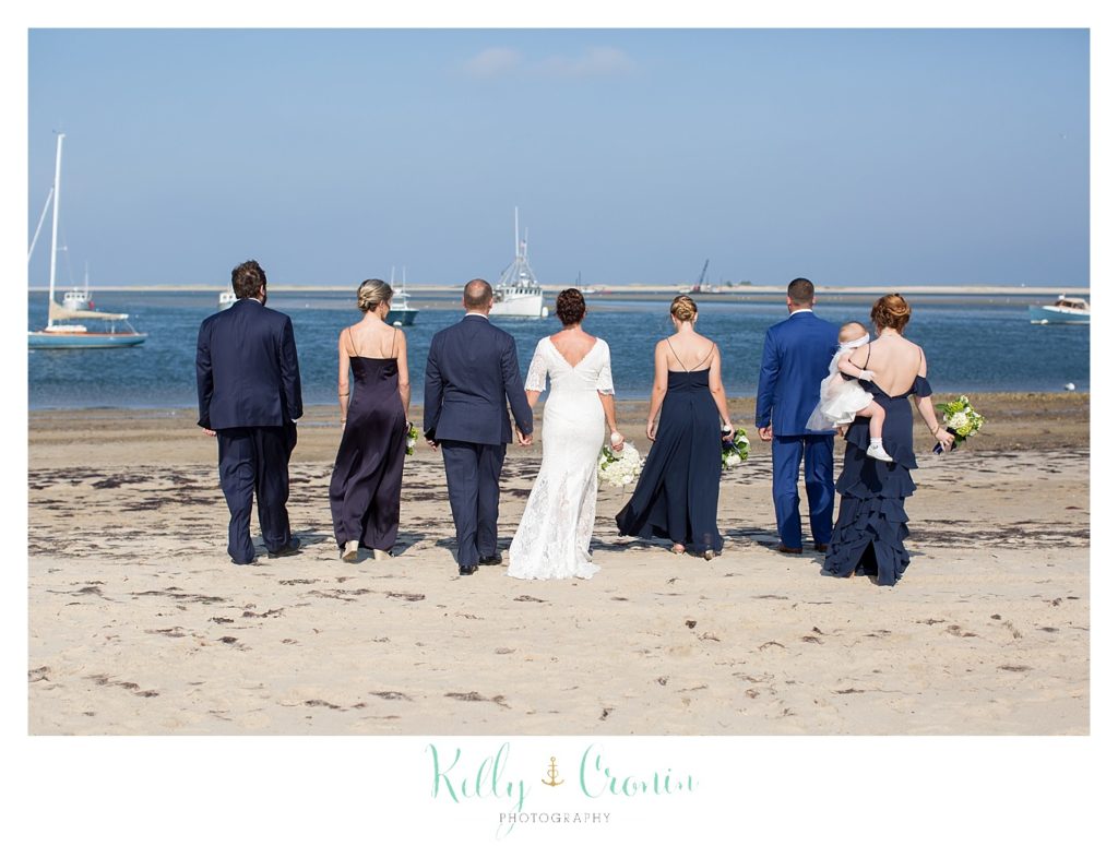 A bridal party stands on teh beach. 