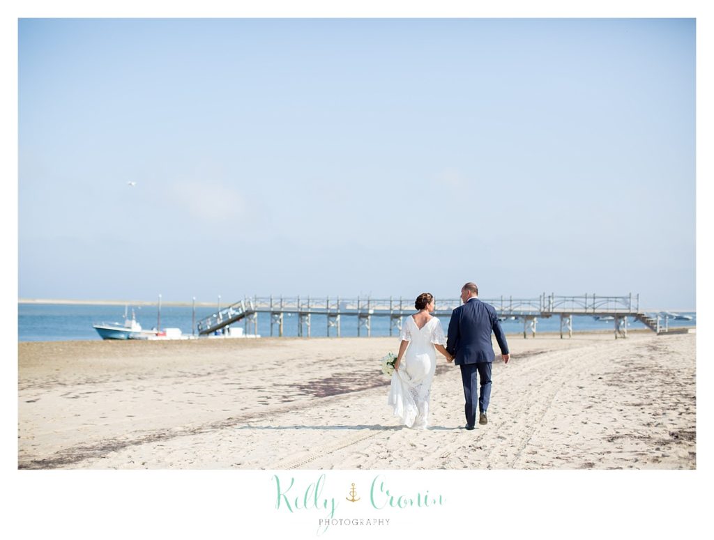 A bride and groom take a walk on the beach. 