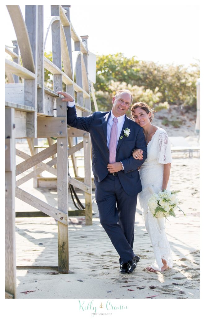 A wedded couple stand next to a pier. 