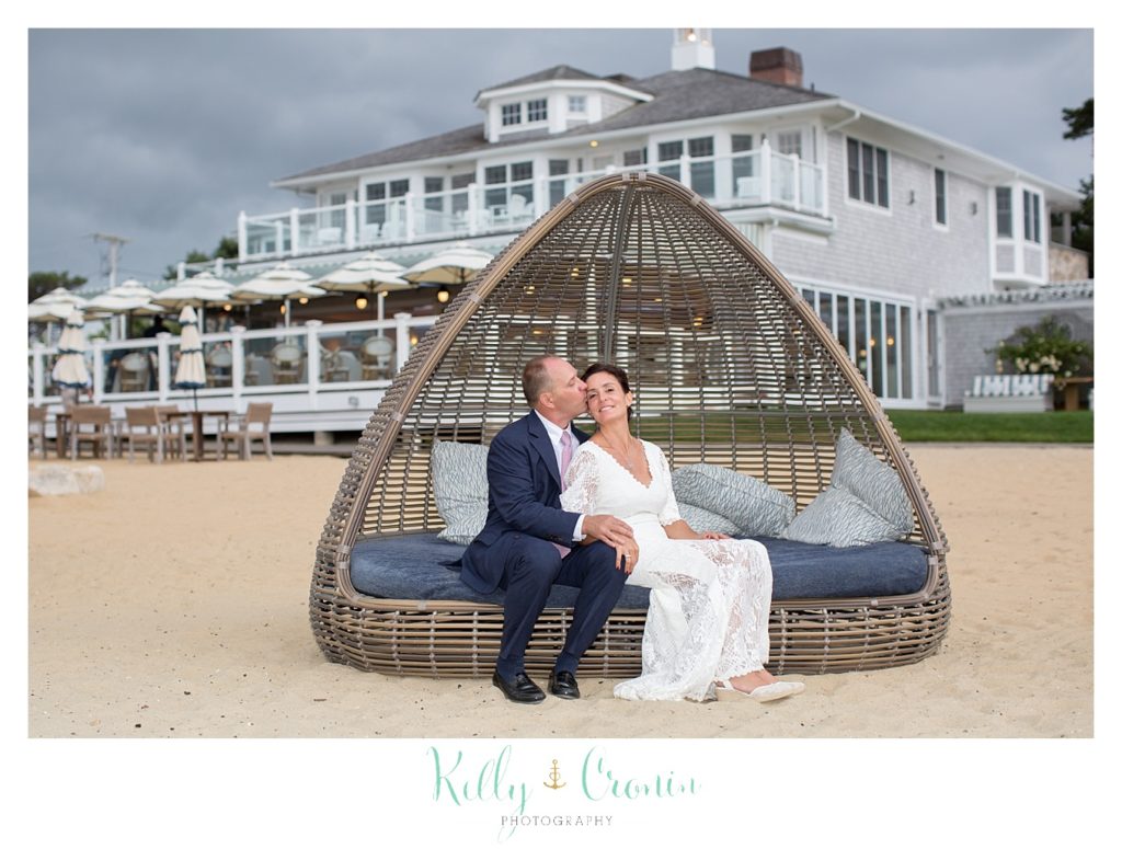 A bride and groom sit on a bungalow on a beach.  
