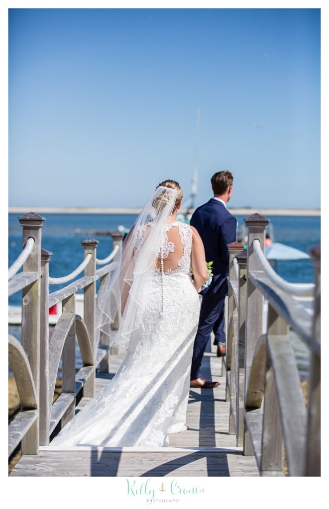 A bride walks up behind her groom on a pier. 