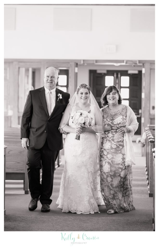 Two older parents walk their daughter down her wedding aisle. 