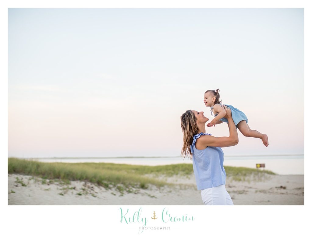 A mom holds her daughter up in the air. 