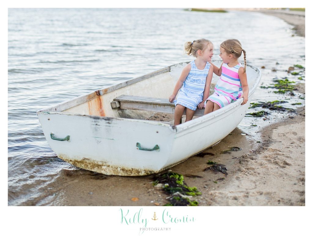 Two sisters sit on a beached boat. 