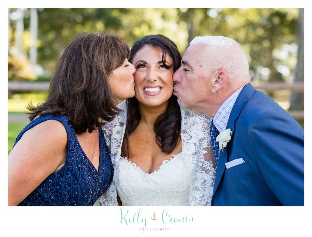 A bride gets a kiss from her parents. 