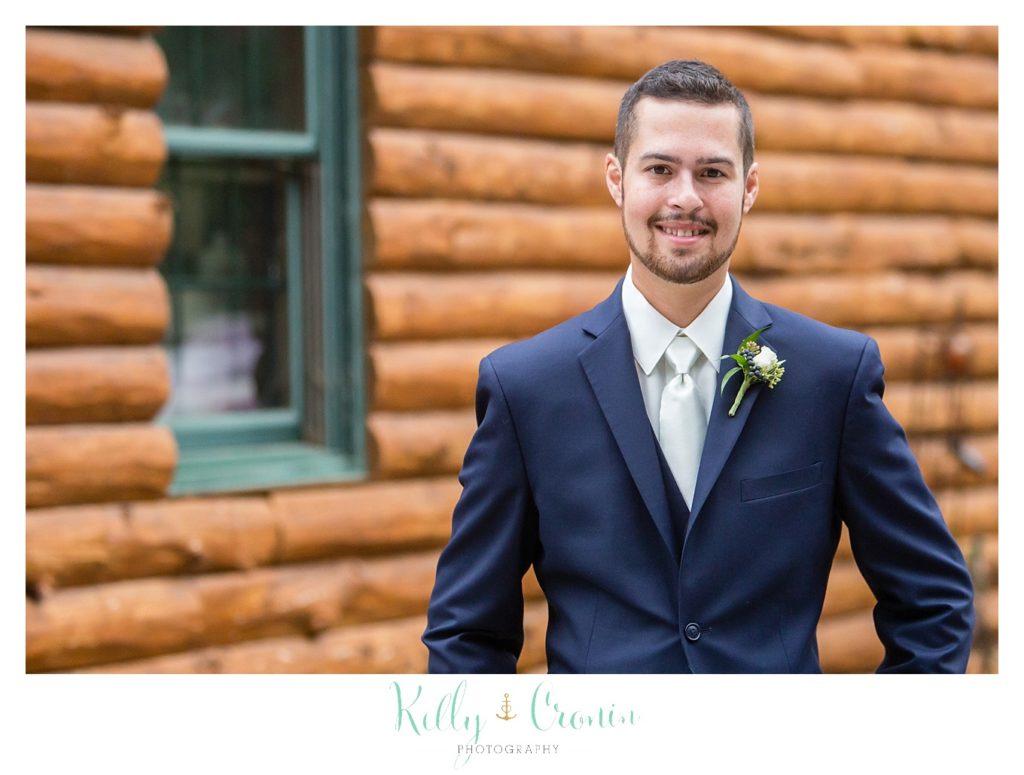A groom poses by a cabin. 