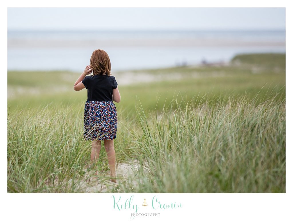 A girl walks through tall grass on the beach. 
