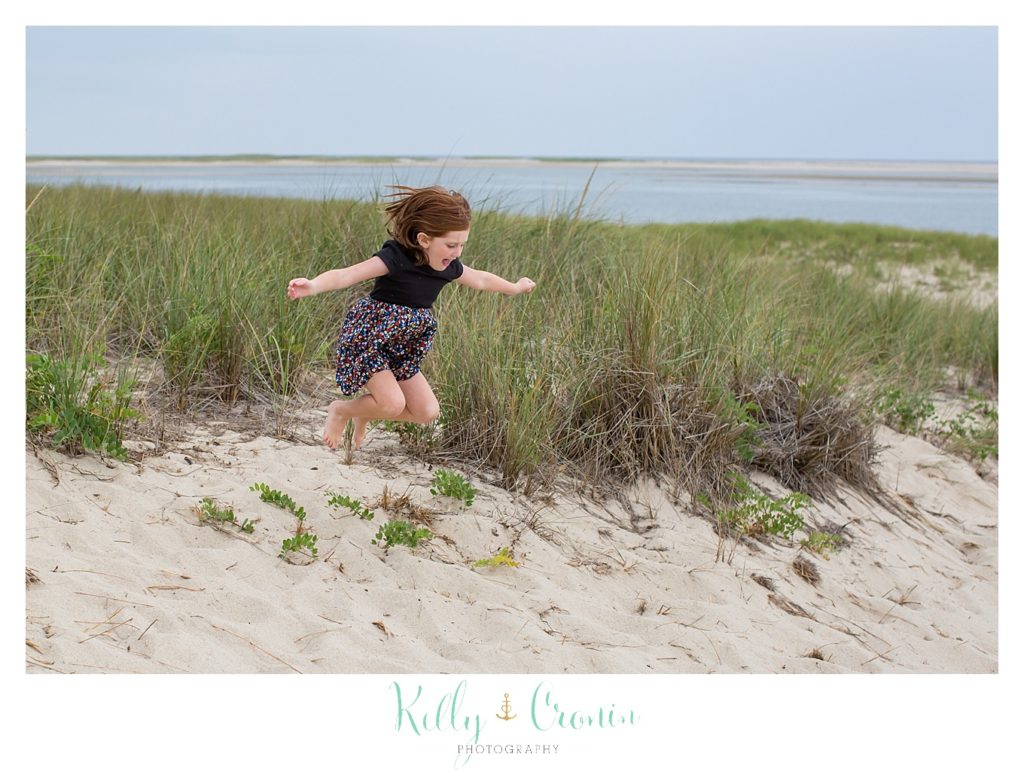 A girl jumps up high in the sand. 